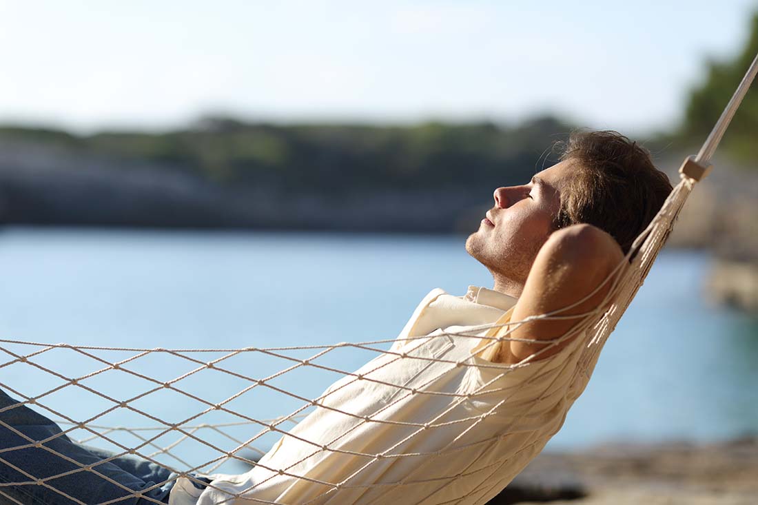 Man relaxing on hammock outside to reduce stress.